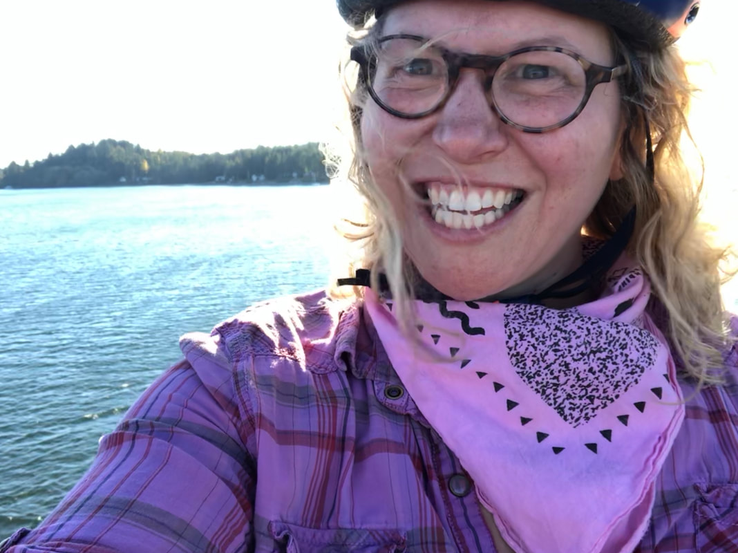 Dr. Hudac smiling in front of water, wearing her bike helmet